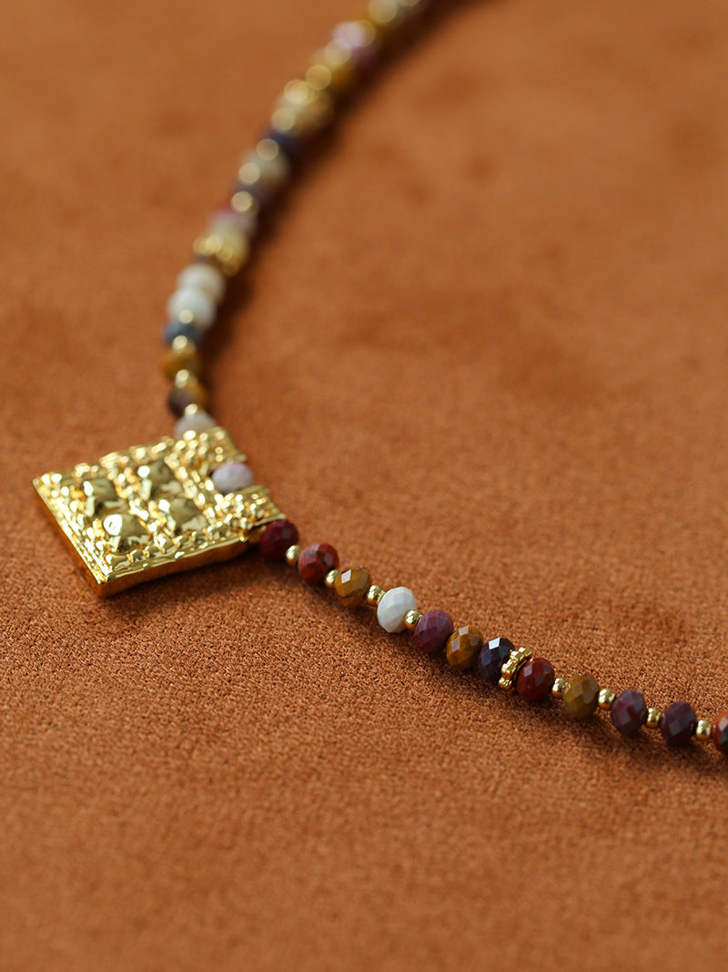 Angled close-up of gold square pendant and stone beads
