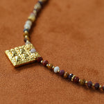 Angled close-up of gold square pendant and stone beads