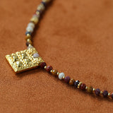 Angled close-up of gold square pendant and stone beads