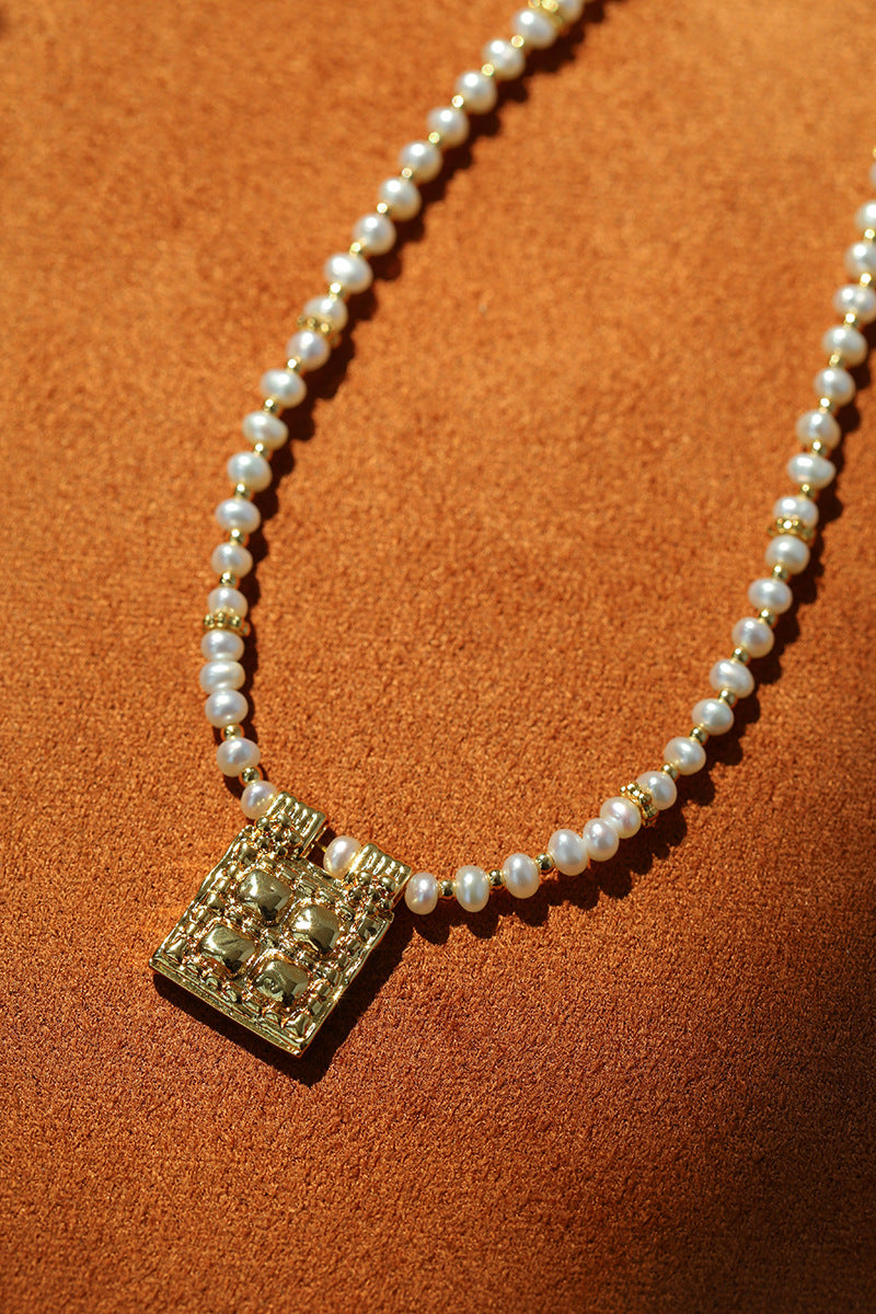 Close-up of textured square pendant on pearl necklace