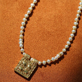 Close-up of textured square pendant on pearl necklace