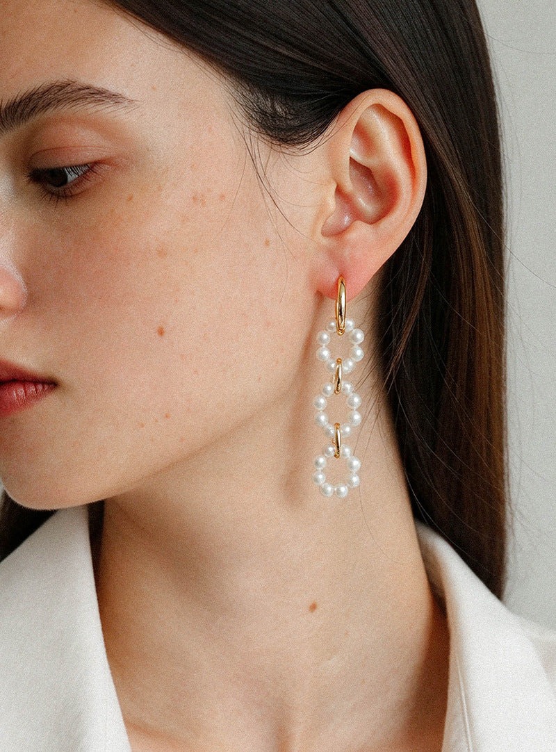 Close-up of long interlocking pearl hoop earrings worn on the ear