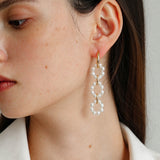Close-up of long interlocking pearl hoop earrings worn on the ear