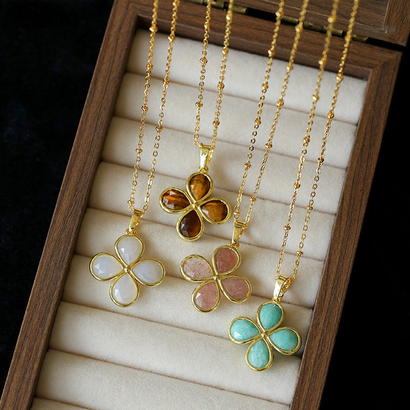 Three gold necklaces with flower-shaped pendants in different colors displayed in a wooden box.