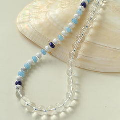 Beaded necklace with blue and purple accents on a beige shell background