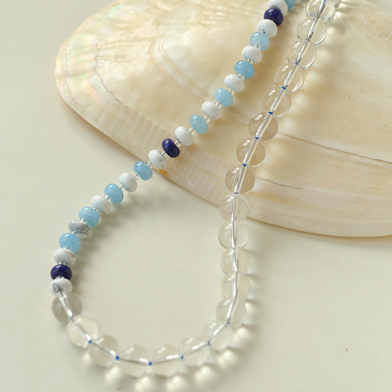 Beaded necklace with blue and purple accents on a beige shell background