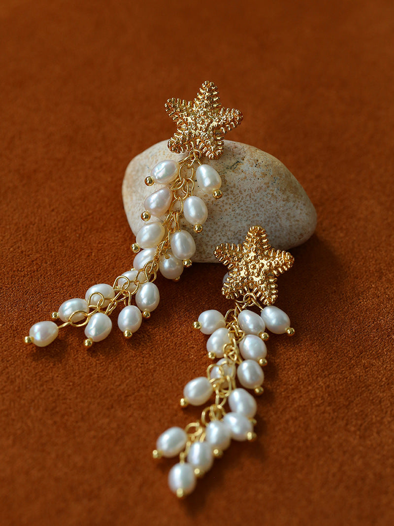 Pair of starfish pearl tassel earrings on a brown background