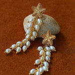 Pair of starfish pearl tassel earrings on a brown background