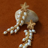 Pair of starfish pearl tassel earrings on a brown background