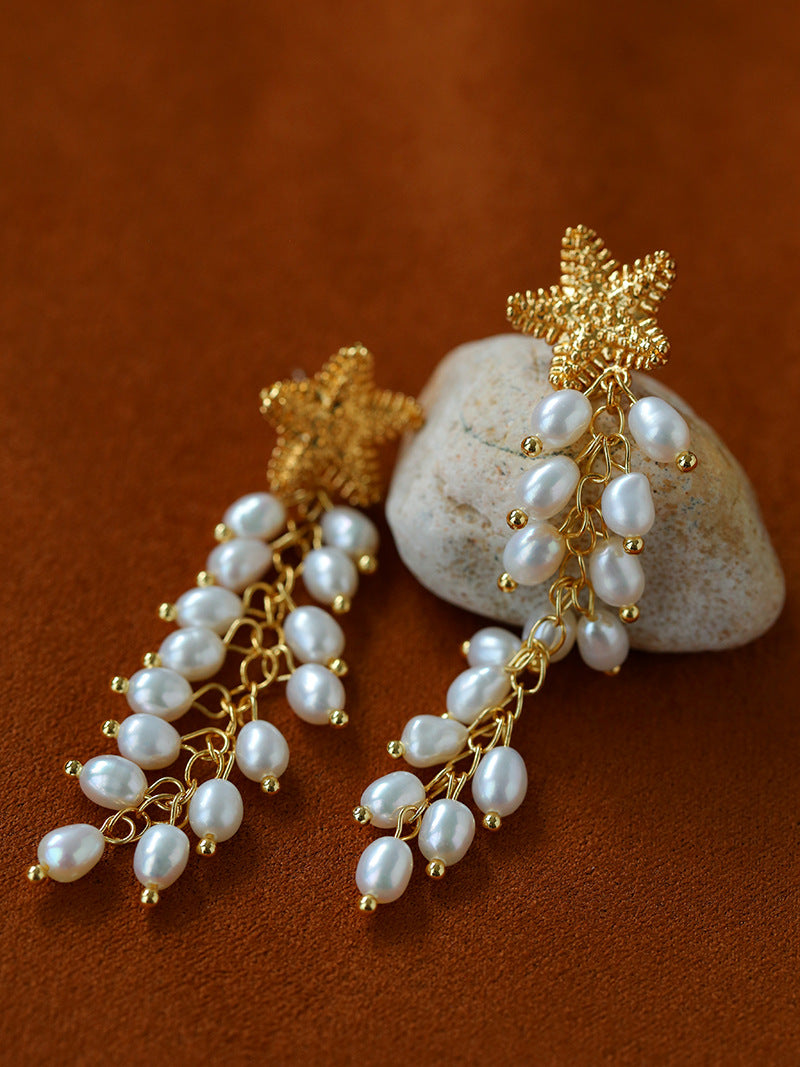 Angled view of gold starfish and pearl tassel earrings