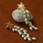 Gold starfish freshwater pearl tassel earrings on a stone display
