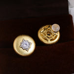 Brushed gold starburst stud earrings on dark display