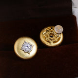 Brushed gold starburst stud earrings on dark display
