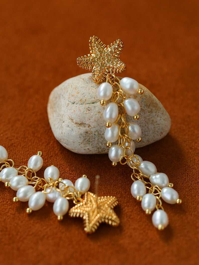 Starfish pearl tassel earrings arranged beside a stone