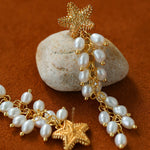 Starfish pearl tassel earrings arranged beside a stone