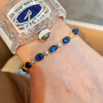 Oval blue sapphire tennis bracelet styled beside a watch